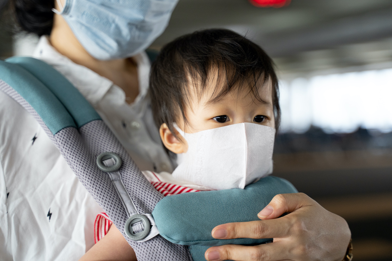 Asian baby with mother in baby carry,baby is wearing a protection mask against air pollution and Wuhan corona covid-19  virus before flight in terminal DonMuang airport,Bangkok, Thailand.