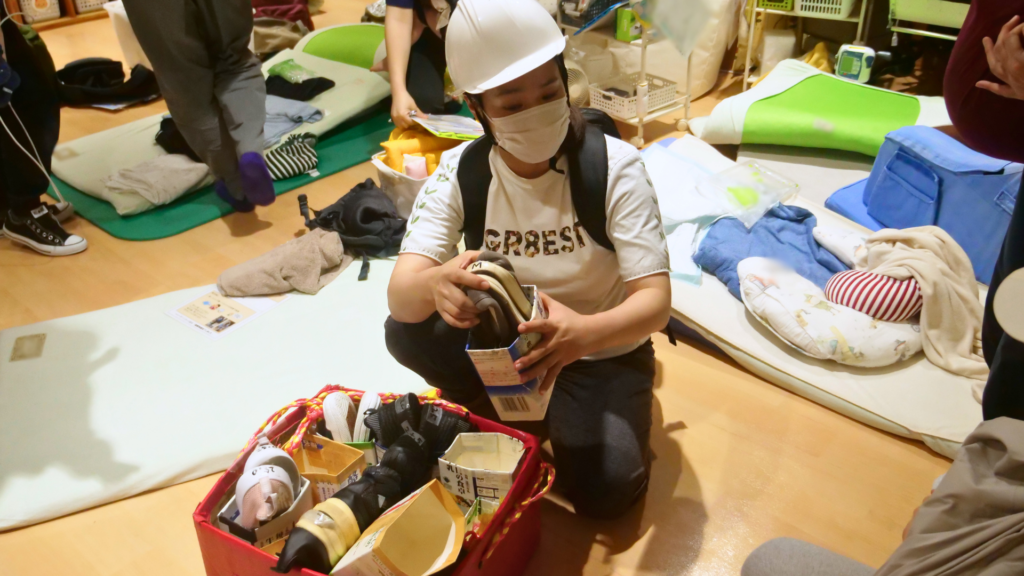避難物品を集める役割のスタッフが避難用の靴を部屋の中央に持っていき、他のスタッフに配っている様子。